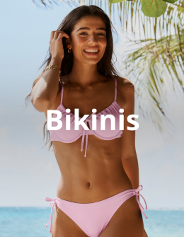 A woman standing under a tree, with one hand in her hair, wearing a pink bikini set from the brand Tropik.