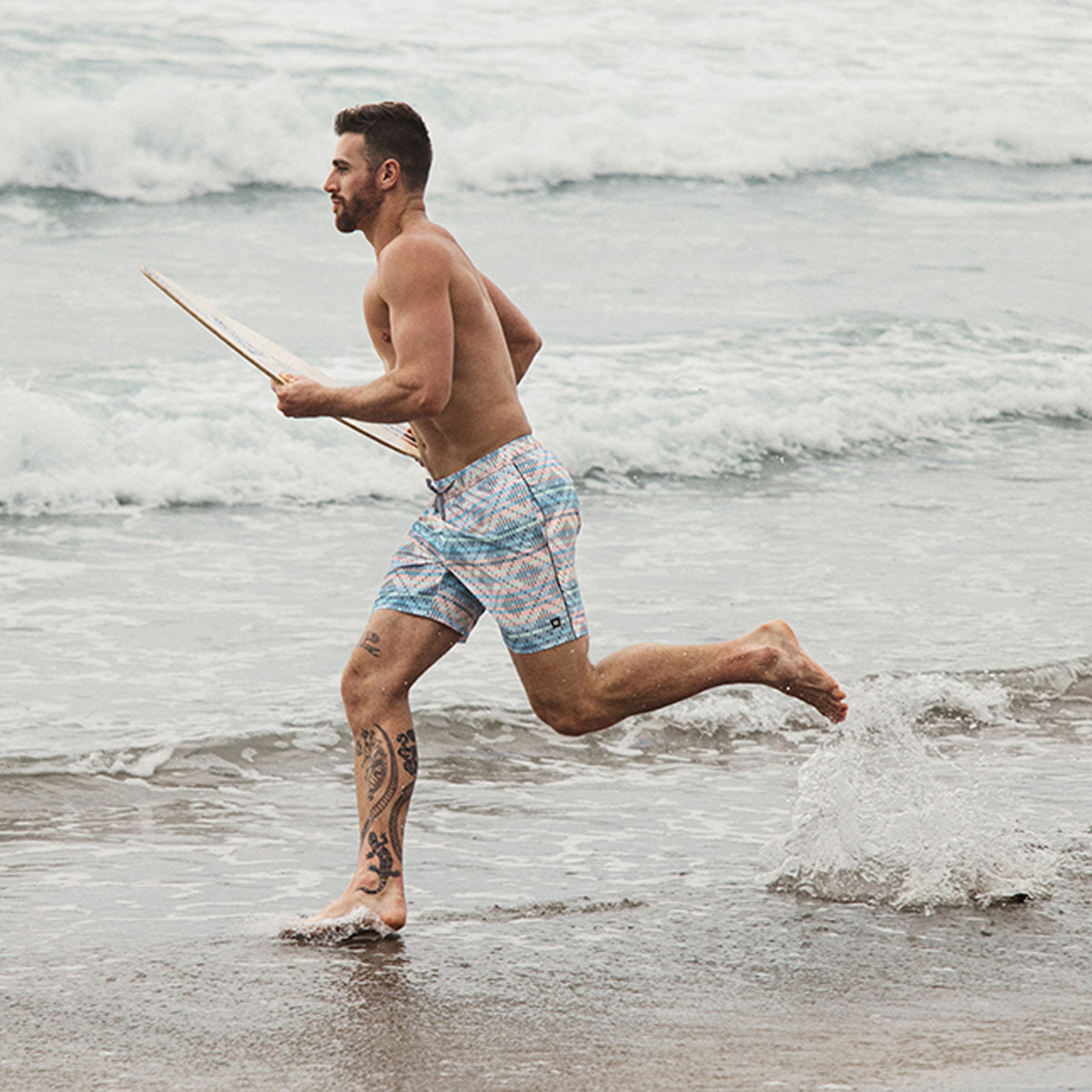 Man running towards the sea with a surf board, wearing a Saxx geometric swimsuit – Bikini  Village  